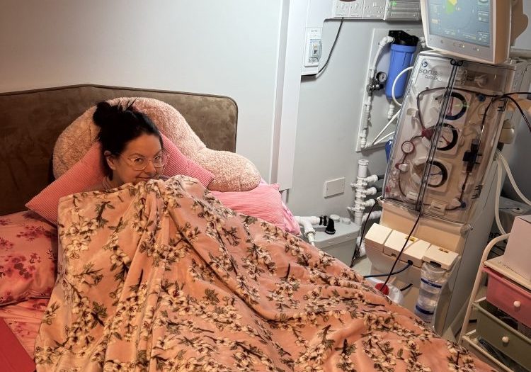 Ellyn Laws Ellyn in bed pulling her duvet up to her face, with dialysis machine next to her.