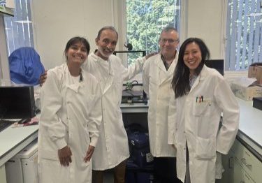 Four researchers in the lab, wearing white lab coats and looking towards the camera